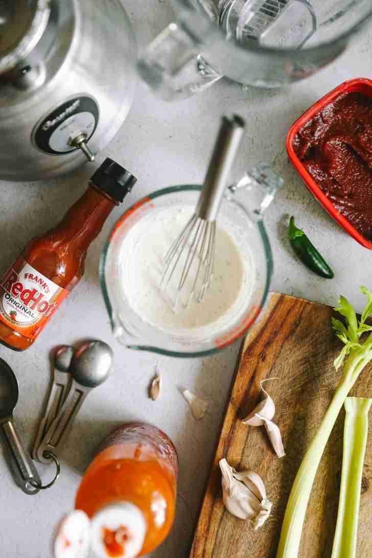 Ingredients for Blue Heat Wing Sauce arranged on a countertop, including Frank's Red Hot, garlic, celery, Sriracha, and bleu cheese dressing in a measuring cup.