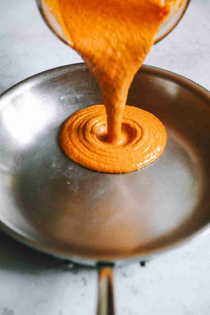 Smooth and creamy Blue Heat Wing Sauce being poured into a stainless steel pan, ready to be simmered and thickened.