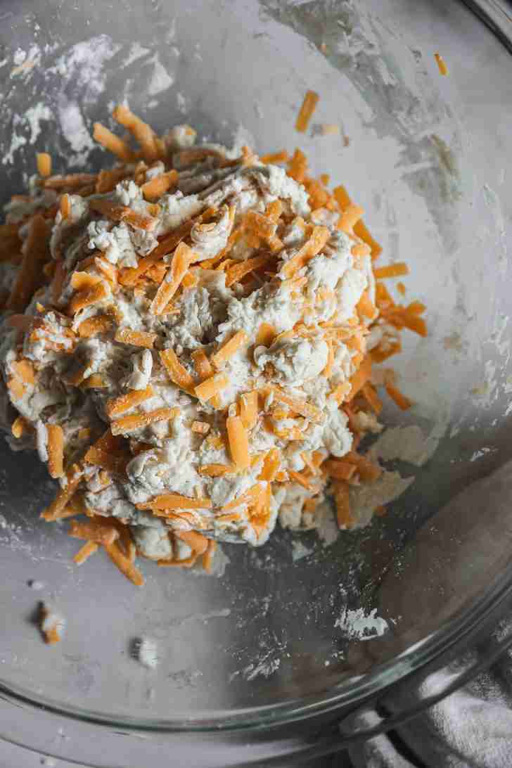 Cheddar cheese being folded into the biscuit dough mixture, creating a cheesy, flaky texture