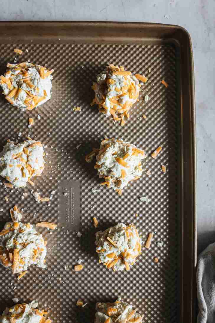 Scoops of unbaked cheddar biscuit dough arranged on a baking sheet, ready to go into the oven.