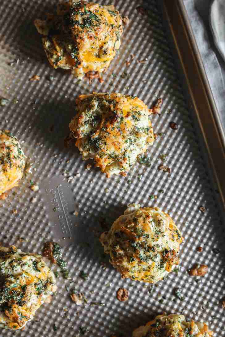 Golden biscuits with garlic and parsley butter brushed on top, resting on a baking sheet with a slightly textured surface.