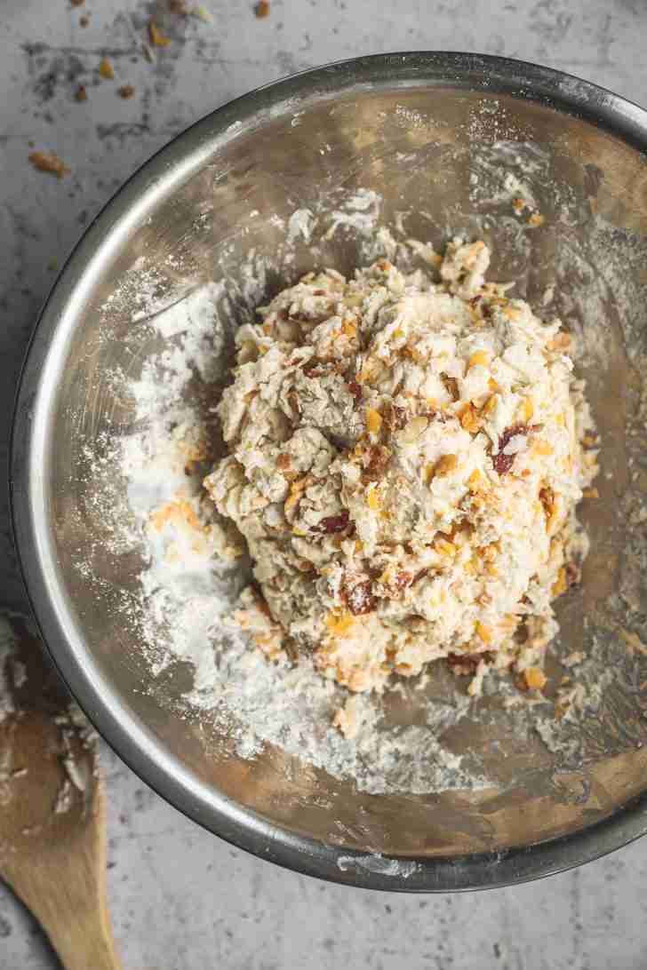 The biscuit dough is now mixed, with cheddar, Gruyère, and bacon bits visible throughout, ready to be shaped into biscuits for baking.