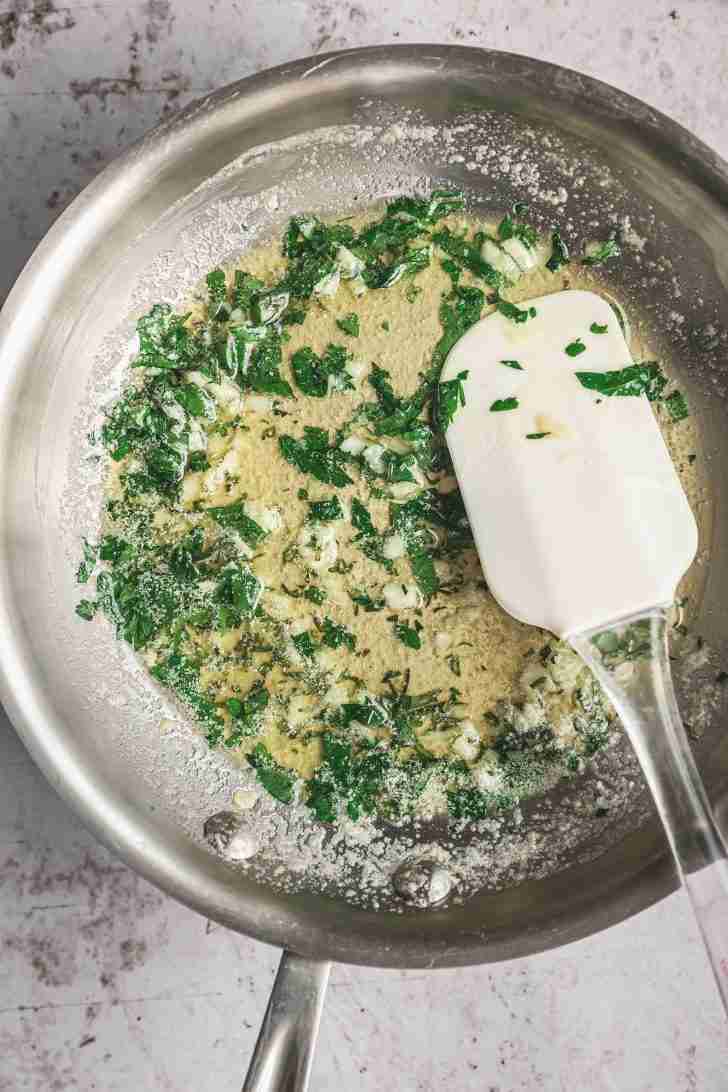 A pan of melted butter is mixed with fresh minced garlic, chopped parsley, and rosemary, creating a fragrant, golden garlic herb butter.