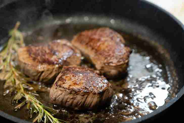 Three perfectly seared steaks cooking in a hot skillet, with fresh rosemary sprigs adding an aromatic touch as they sizzle in bubbling oil.