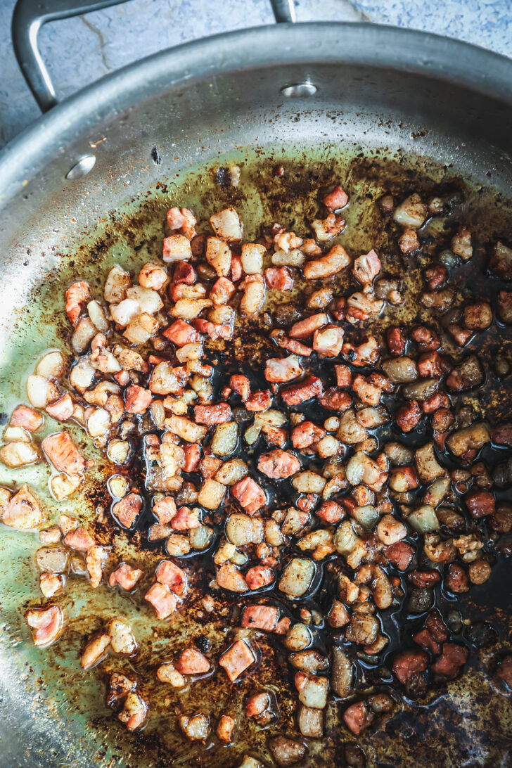 Diced pancetta cooking in a skillet until golden and crispy, leaving rendered fat and caramelized bits behind.