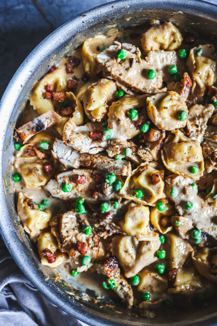 Chicken tortellini in a creamy Alfredo sauce with peas, pancetta, and sliced chicken, garnished and ready to serve.