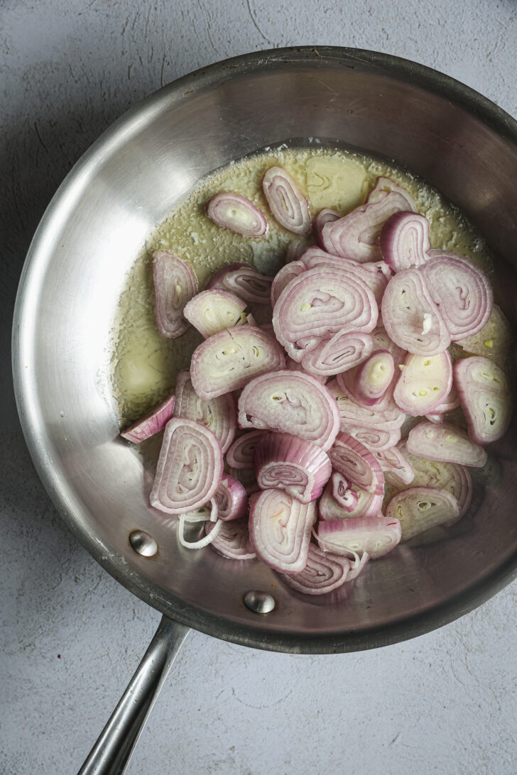 Sliced shallots in melted butter in a stainless steel skillet, ready to be caramelized for the vodka sauce.