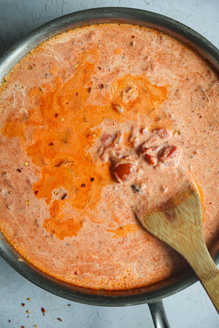 Creamy vodka sauce simmering in a skillet, blending tomatoes, cream, and chili flakes with a wooden spatula stirring the mixture