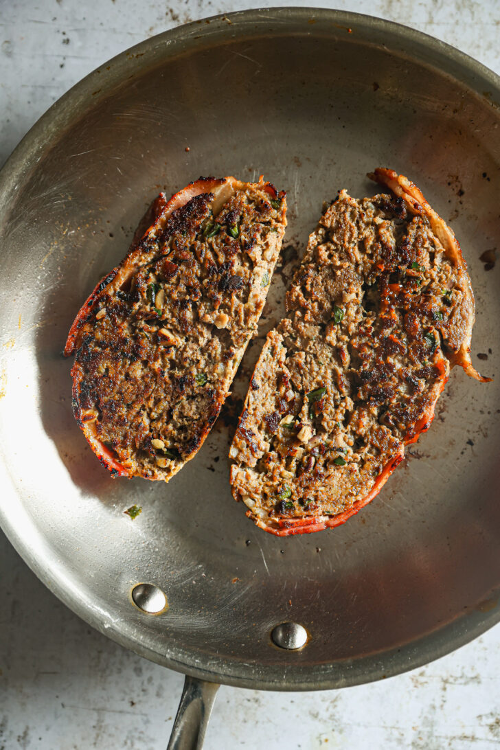 Two slices of meatloaf seared to perfection in a skillet, showcasing a crispy browned crust and a tender, herb-filled interior.