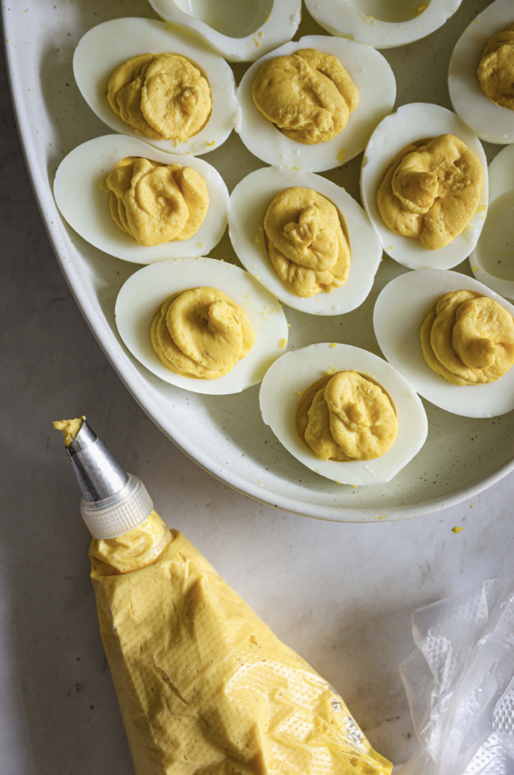 Deviled egg filling piped into halved egg whites using a pastry bag, arranged on a white platter