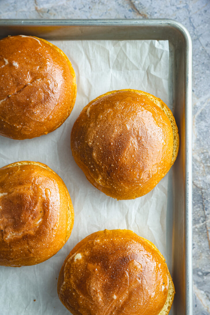 Golden brioche buns brushed with garlic aioli, resting on parchment-lined baking sheet, ready for toasting