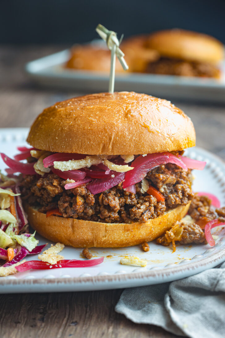 Sloppy Joe sandwich on a toasted brioche bun, topped with pickled onions and crispy fried onions, se