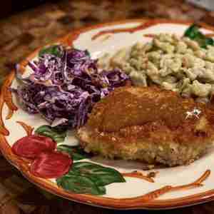 Pork schnitzel topped with sauce, served with purple cabbage slaw and spaetzle on a decorative plate with red apples.