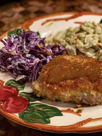 Pork schnitzel topped with sauce, served with purple cabbage slaw and spaetzle on a decorative plate with red apples.