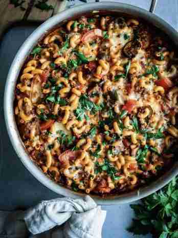 A large pot of beefaroni, topped with fresh parsley and melted cheese, featuring macaroni pasta, beef, and vegetables in a rich tomato sauce.