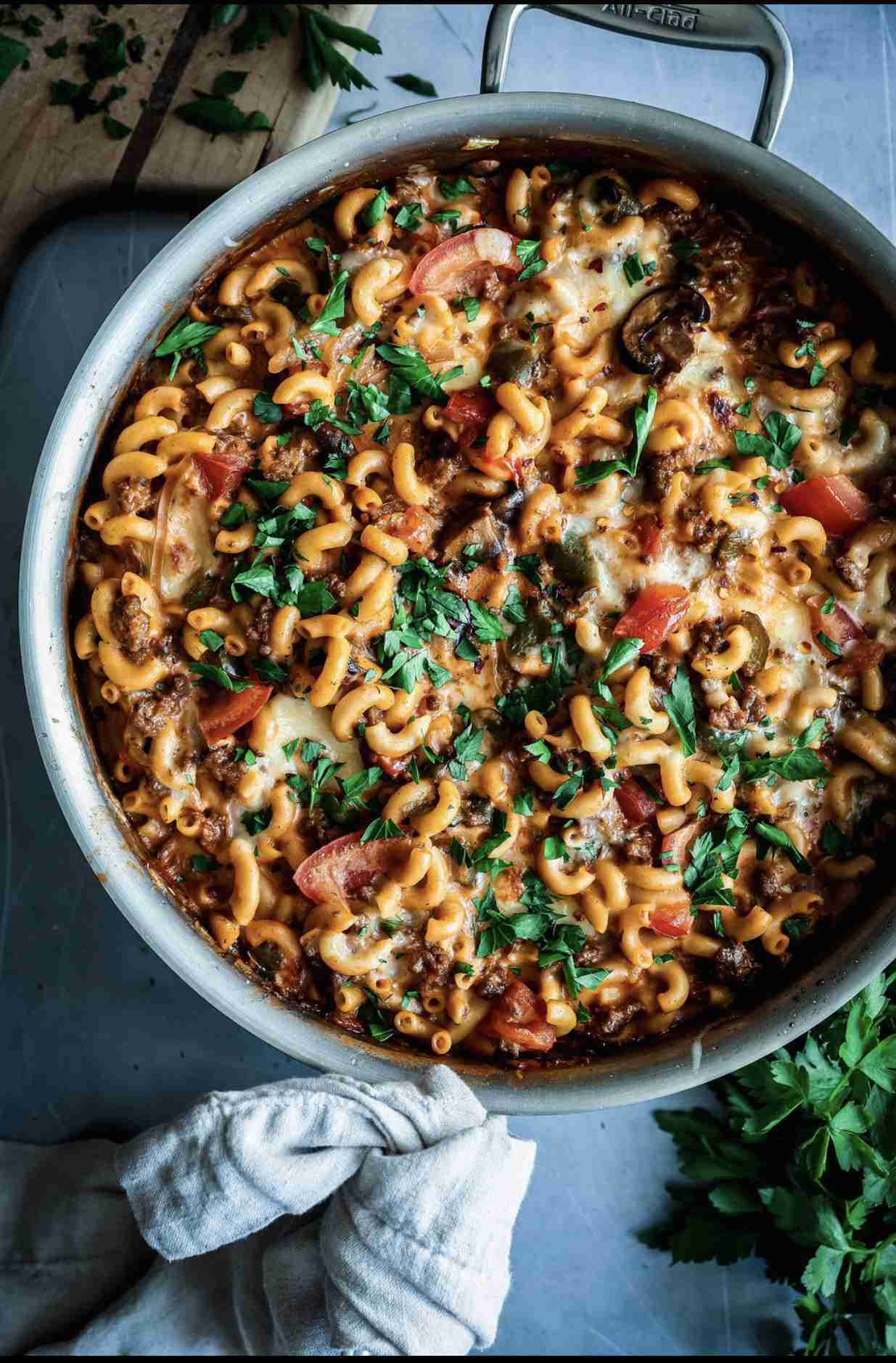 A large pot of beefaroni, topped with fresh parsley and melted cheese, featuring macaroni pasta, bee