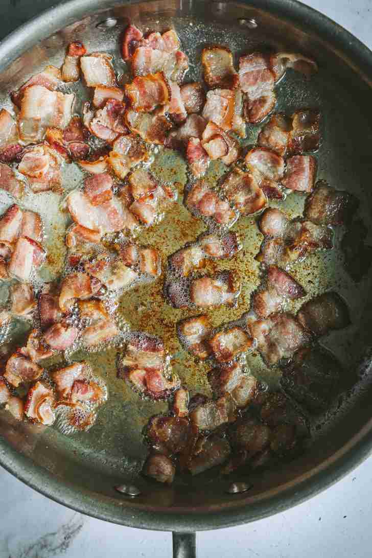 Crispy bacon pieces frying in a pan, sizzling in their own fat, with browned edges and bubbling grease.