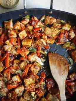 A skillet filled with stir-fried pork, red bell peppers, celery, and green onions coated in a glossy gochujang sauce, topped with sesame seeds.