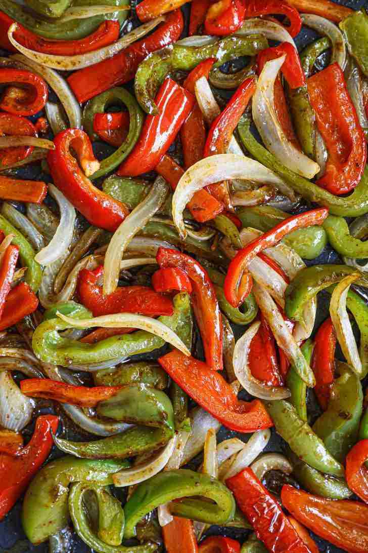 A close-up view of sautéed red and green bell peppers mixed with sliced onions. The vegetables are coated in a rich seasoning, giving them a glossy, slightly caramelized appearance. The peppers are vibrant, and the onions have softened and turned golden, with some edges slightly charred, adding depth to the overall flavor. The mix of colors and textures makes the dish look fresh and inviting.