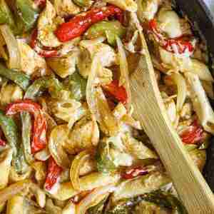 A skillet of creamy chicken fajita pasta with colorful bell peppers, onions, chicken, and penne, all mixed with a rich, cheesy sauce.