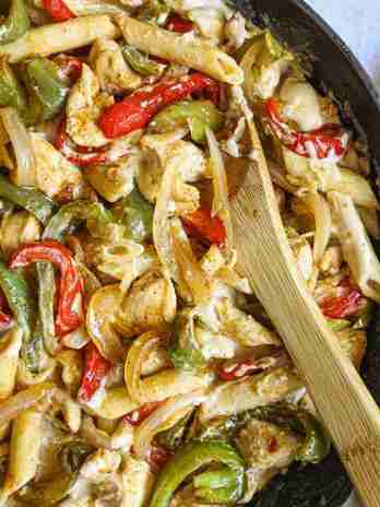 A skillet of creamy chicken fajita pasta with colorful bell peppers, onions, chicken, and penne, all mixed with a rich, cheesy sauce.