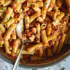 Cooked ziti pasta is coated in a rich tomato blue cheese sauce, garnished with fresh herbs and served in a large pan with a spoon ready for serving.