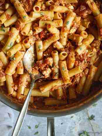 Cooked ziti pasta is coated in a rich tomato blue cheese sauce, garnished with fresh herbs and served in a large pan with a spoon ready for serving.