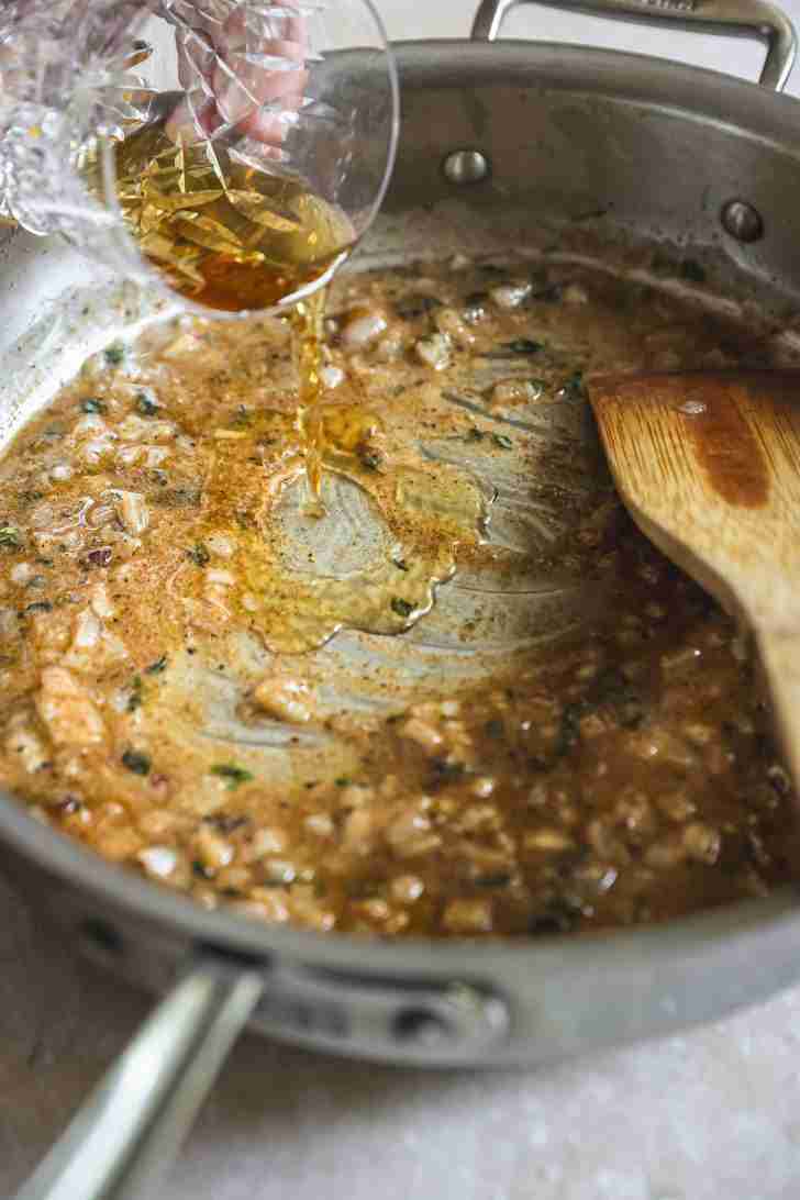 Brandy being poured into a skillet with sautéed onions and spices, deglazing the pan to create a flavorful base for sauce.