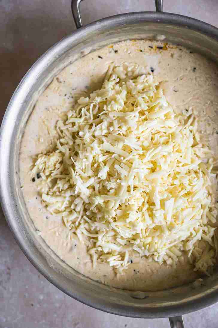 Shredded cheese piled into a creamy sauce base in a skillet, ready to be melted for a rich, cheesy mac and cheese sauce.