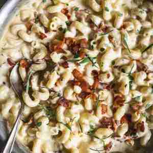 Finished bacon brandy mac and cheese in a skillet, creamy and topped with crispy bacon and fresh herbs, ready to serve.