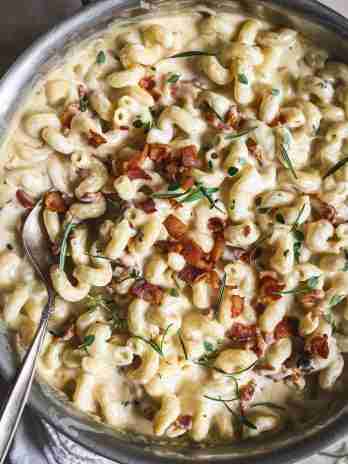 Finished bacon brandy mac and cheese in a skillet, creamy and topped with crispy bacon and fresh herbs, ready to serve.