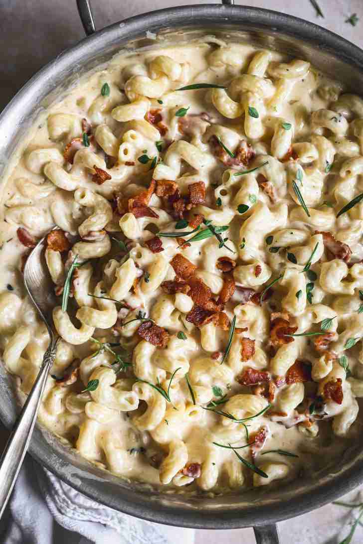 Finished bacon brandy mac and cheese in a skillet, creamy and topped with crispy bacon and fresh herbs, ready to serve.