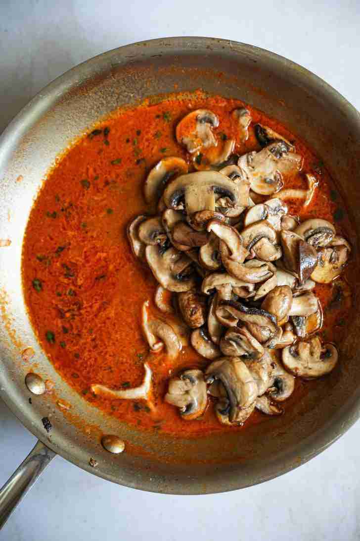 Sliced mushrooms added to a skillet with a rich, red Madeira wine sauce, simmering together to create the mushroom wine sauce.