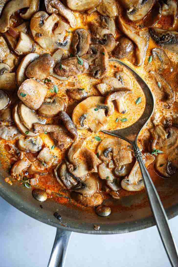 Close-up of creamy mushroom Madeira wine sauce in a skillet, garnished with fresh thyme, ready to be spooned over filet mignon.