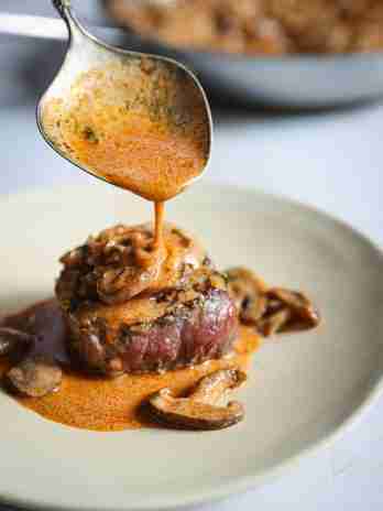 Rich Madeira mushroom wine sauce being spooned over perfectly cooked filet mignon steaks, garnished with fresh thyme and mushrooms, ready to serve.