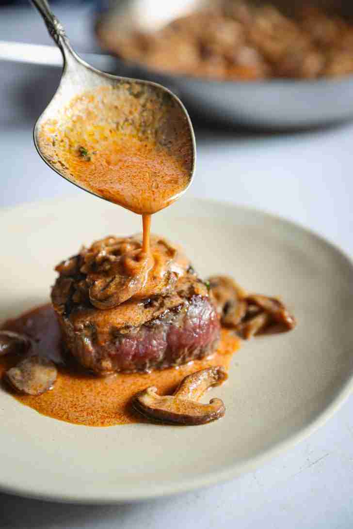 Rich Madeira mushroom wine sauce being spooned over perfectly cooked filet mignon steaks, garnished with fresh thyme and mushrooms, ready to serve.