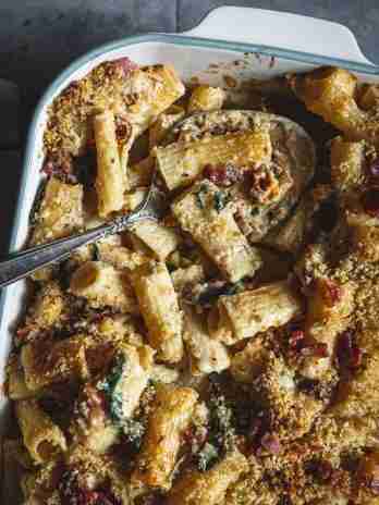 Baked mac and cheese with rigatoni, crispy breadcrumbs, and bacon, topped with a golden crust in a white baking dish, ready to serve.