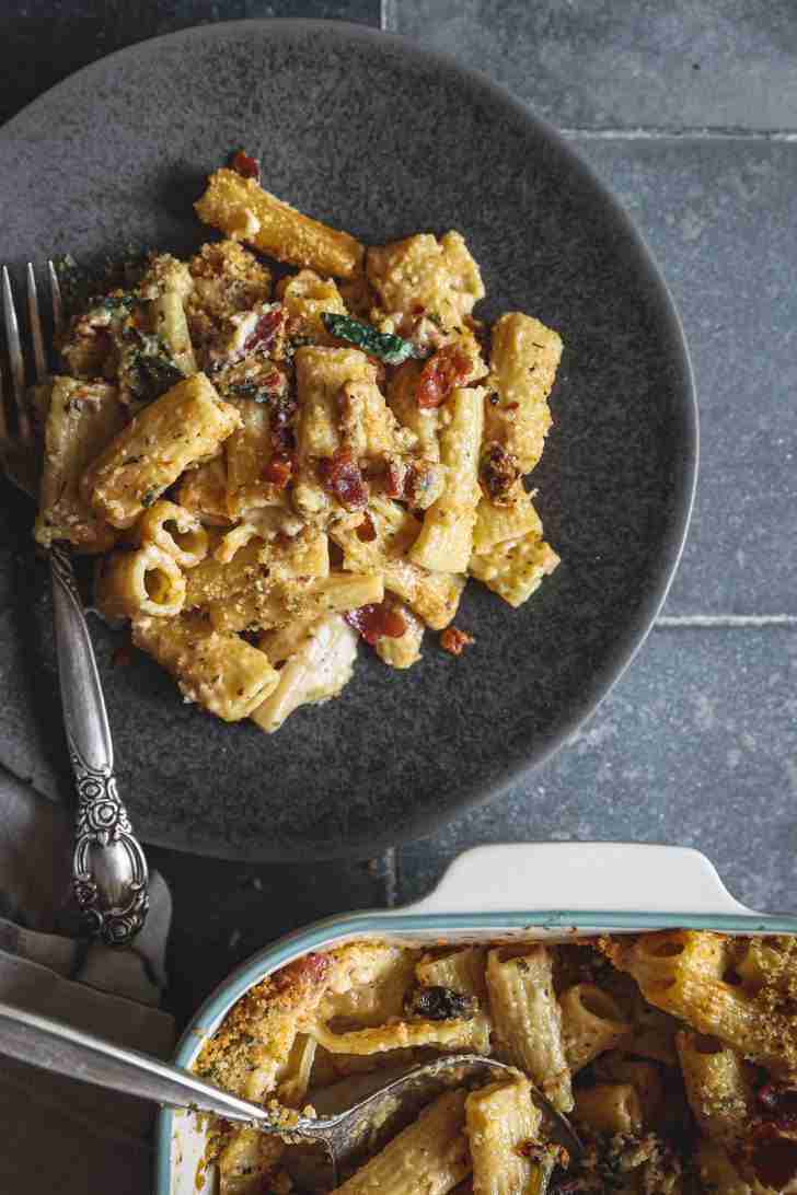 Plate of baked mac and cheese with rigatoni, crispy bacon, and creamy cheese sauce, next to a casserole dish of the same dish topped with breadcrumbs.