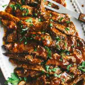 Tender, sliced brisket coated in a rich BBQ sauce, garnished with fresh parsley on a white serving platter, ready to be served.