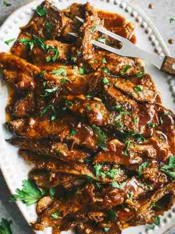 Tender, sliced brisket coated in a rich BBQ sauce, garnished with fresh parsley on a white serving platter, ready to be served.