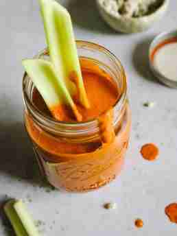 A jar filled with Blue Heat Wing Sauce has celery sticks inserted, with sauce drips on the side of the jar and some splatters on the countertop.