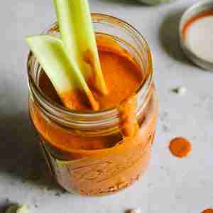 A jar filled with Blue Heat Wing Sauce has celery sticks inserted, with sauce drips on the side of the jar and some splatters on the countertop.