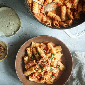 Bowls of rigatoni in creamy vodka sauce topped with fresh basil and Parmesan, served alongside a skillet of pasta and chili flakes.