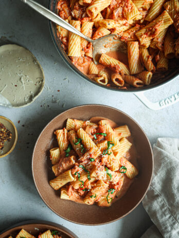 Bowls of rigatoni in creamy vodka sauce topped with fresh basil and Parmesan, served alongside a skillet of pasta and chili flakes.