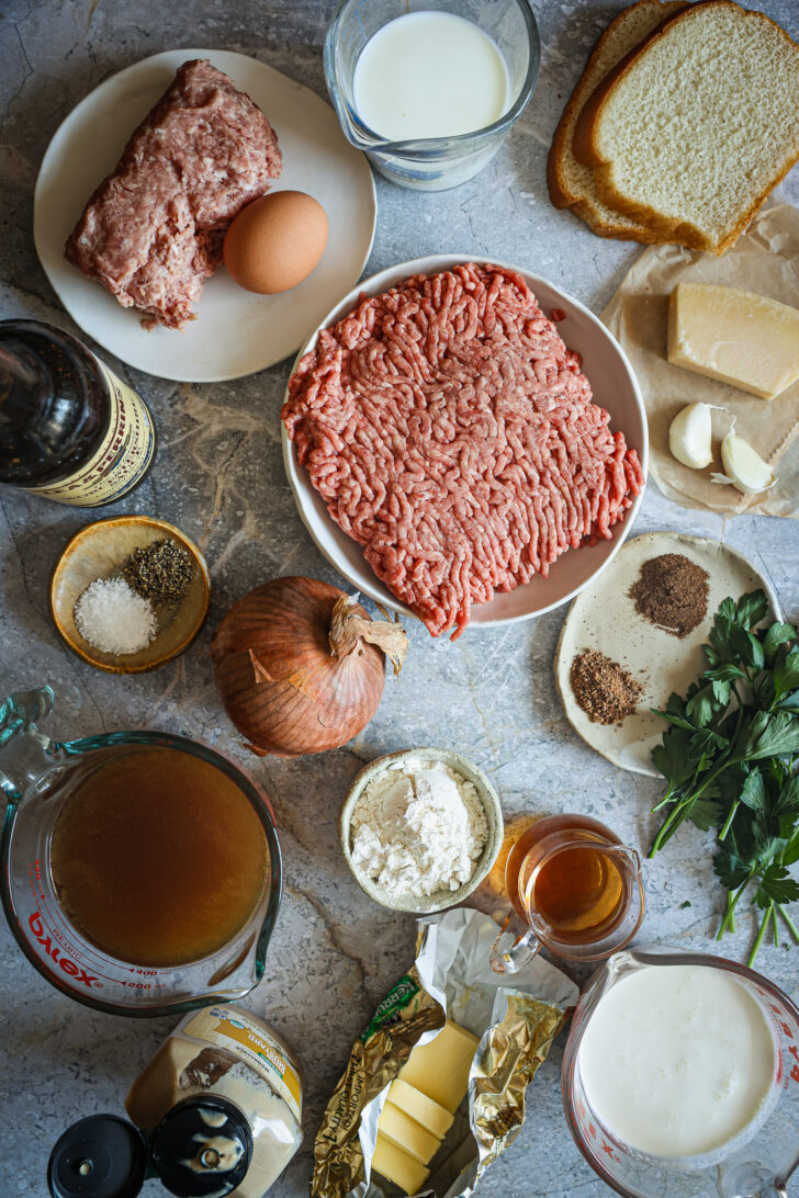 Ingredients for Swedish meatballs arranged on a countertop, including ground meats, onion, bread, milk, butter, and seasonings.