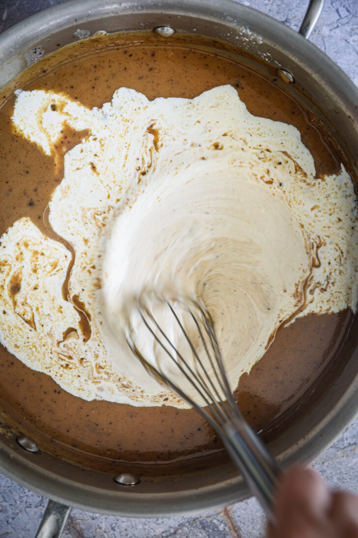 Cream being whisked into rich brown gravy in a skillet, creating a smooth and creamy sauce for the Swedish meatballs.