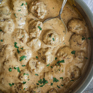 Swedish meatballs simmered in creamy gravy, garnished with fresh parsley, with a serving spoon in the skillet.