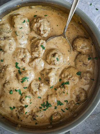 Swedish meatballs simmered in creamy gravy, garnished with fresh parsley, with a serving spoon in the skillet.