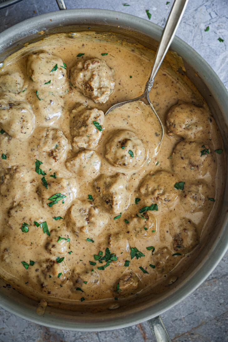 Swedish meatballs simmered in creamy gravy, garnished with fresh parsley, with a serving spoon in the skillet.