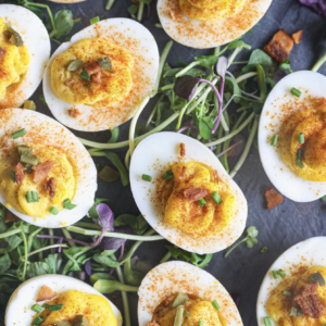 Deviled eggs garnished with paprika, chives, crispy bacon, and pickles, served on a bed of fresh microgreens for extra color